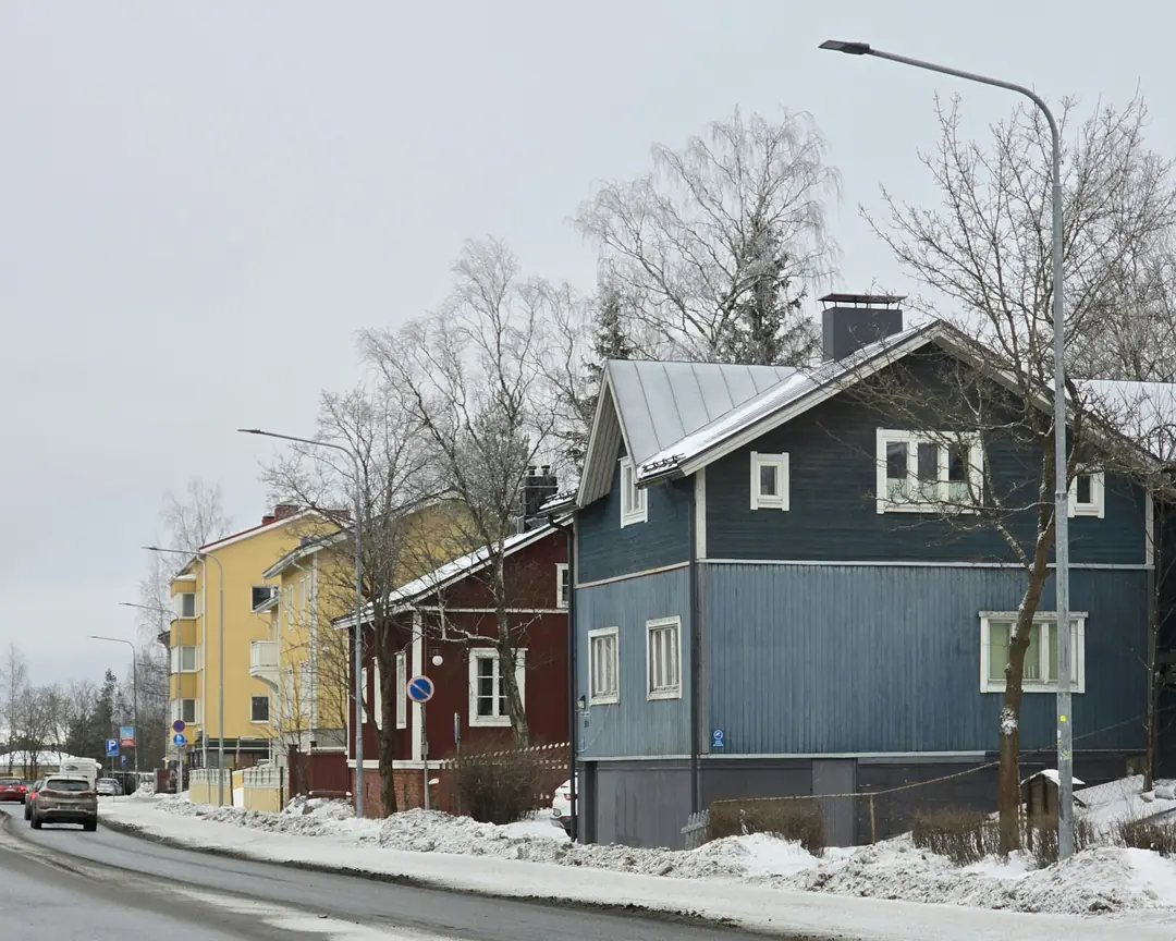 Puutaloja ja kerrostalo lumisen kadun varrella talvella