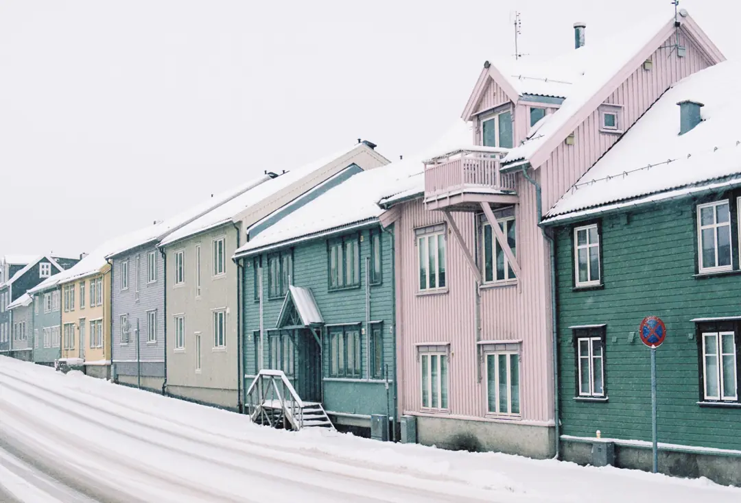 Värikkäitä puisia asuinrakennuksia lumisen kadun varrella