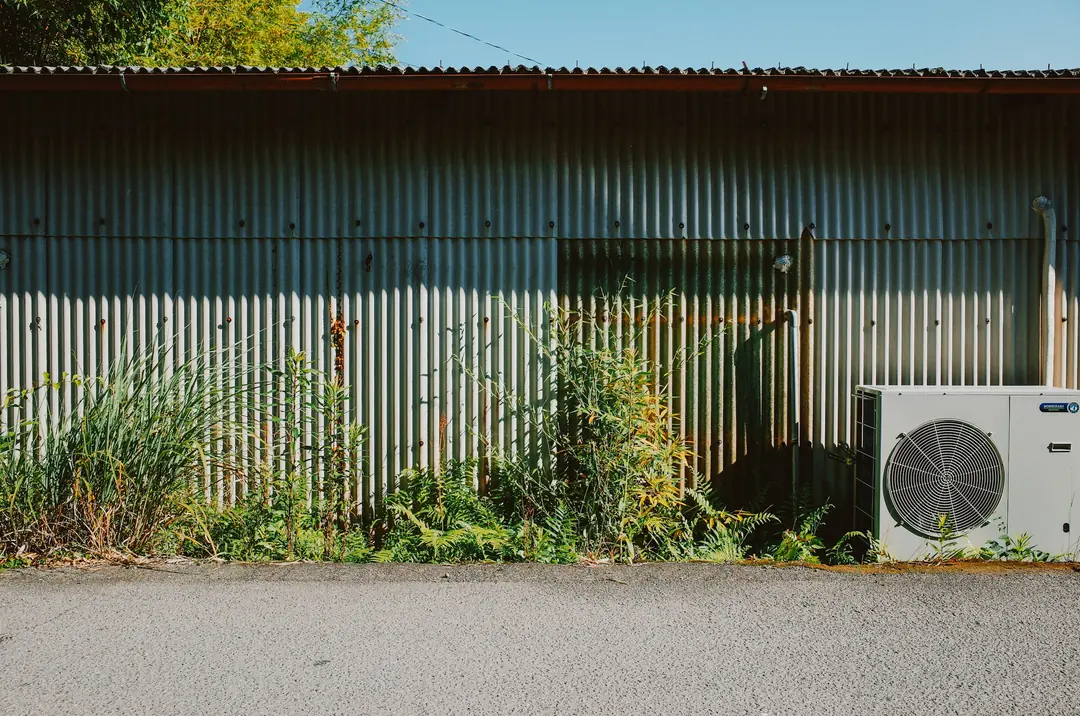 Ilmalämpöpumpun ulkoyksikkö peltiseinän vieressä